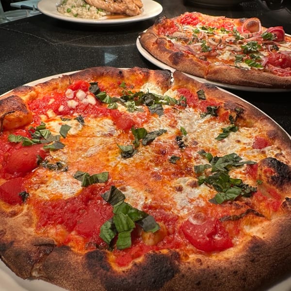 Two delicious Luna Rossa Italian pizzas with fresh basil, tomatoes, and cheese on a dark table.