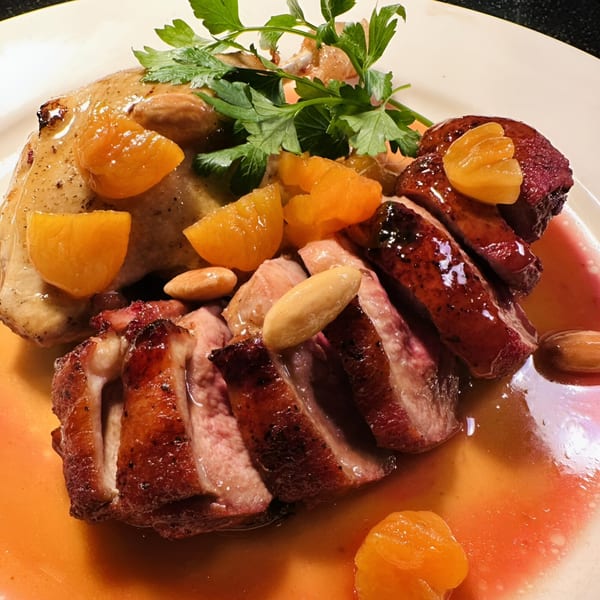 Roasted duck with apricots, almonds, and parsley in a rich sauce on a white plate.