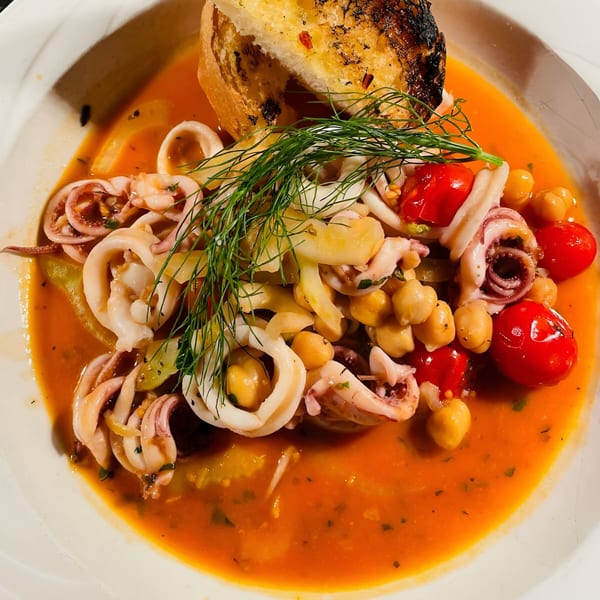 Calamari stew with chickpeas, cherry tomatoes, and dill in a rich tomato broth, served with garlic bread.