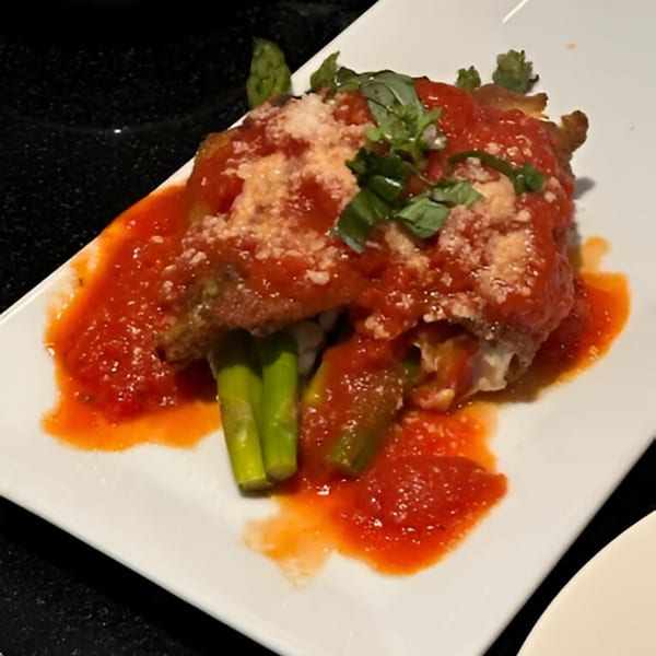 Italian dish with red sauce, parmesan, and basil, served with asparagus on a white plate.
