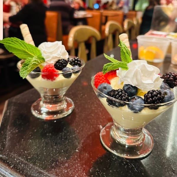 Two Luna Rossa desserts with whipped cream, berries, and mint in glass cups on a dark counter.