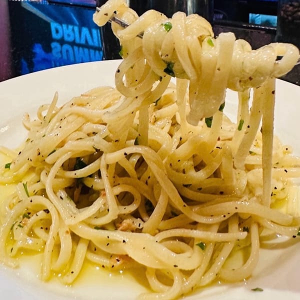 Fork lifting spaghetti with olive oil, garlic, and herbs from a white plate at Luna Rossa.